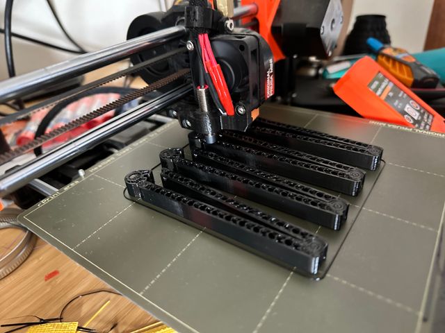 The same batch of four clips with the printhead extruding a layer of plastic over the magnets.