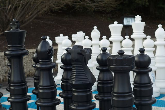 Oversized chess pieces, the size of children, on a blue and white checkerboard floor.