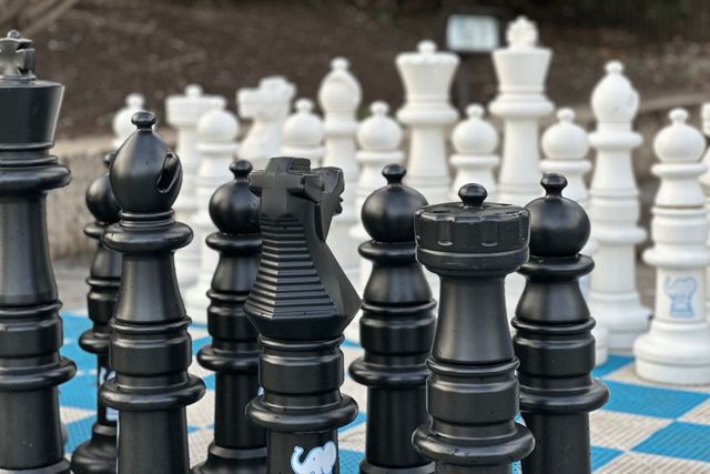 Oversized chess pieces, the size of children, on a blue and white checkerboard floor. The image is slightly brighter, the background is slightly fuzzier, and the pieces have a bit more of a halo.
