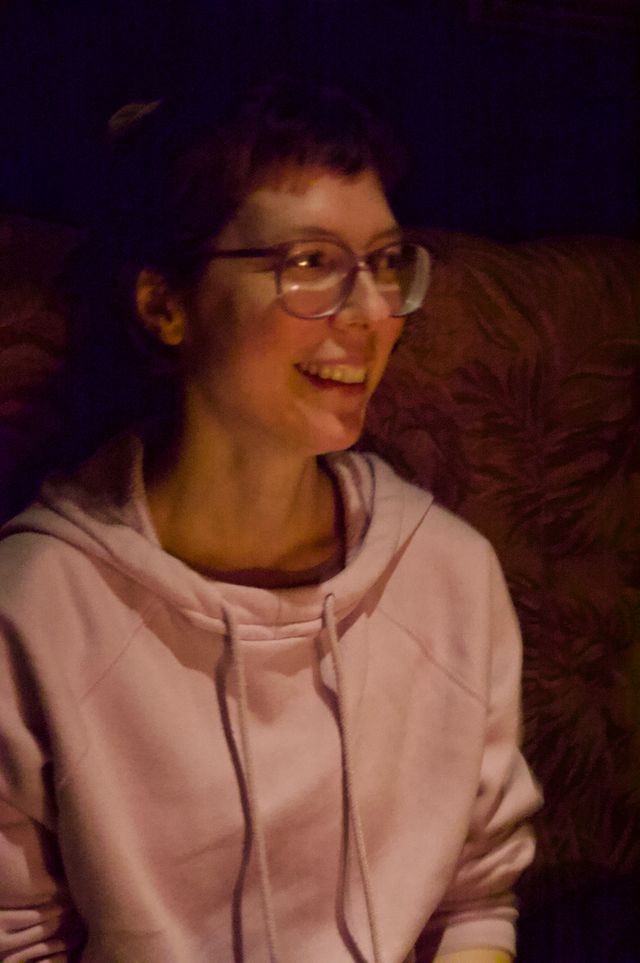 Close up portrait of a brunette woman with glasses. The image is dark warm-toned and a bit blurry.