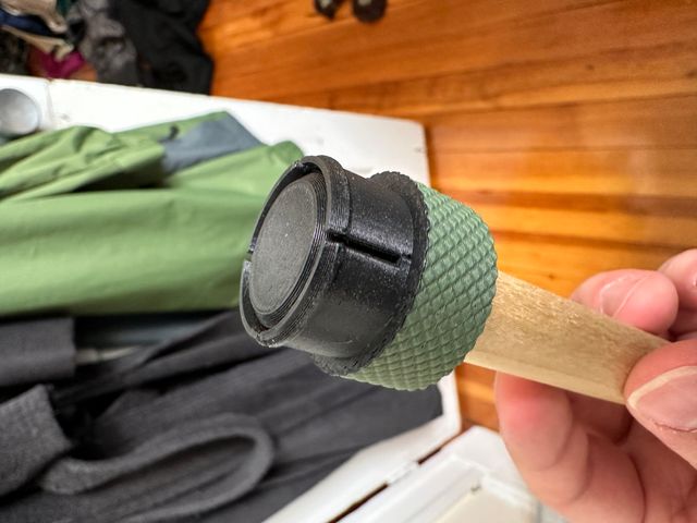 A wooden dowel attached to a cylindrical object with a knurled green cap where the cylinder meets the dowel and on the other side a black snap connector.