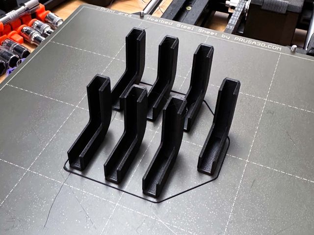 Seven L shaped corner bumpers standing vertically on a 3D printer print bed.