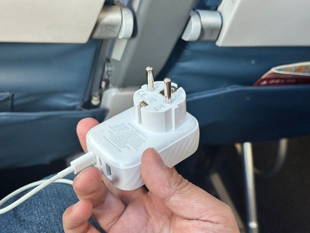 The same white adapter, unplugged and in hand, revealing two cylindrical "European-style" prongs and three USB ports on the underside.