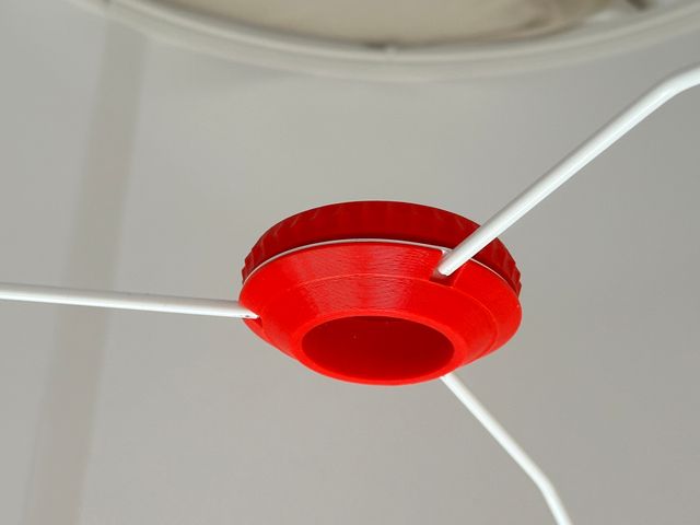 The two red parts screwed together around the frame of a lampshade. Three white metal rods extend from the channels in the red plastic.