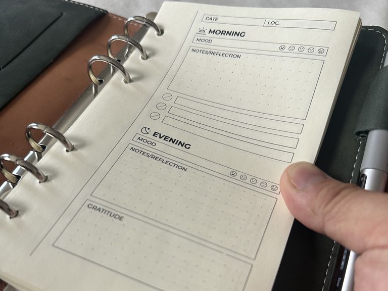 A printed daily page in the ring binder: Morning and Evening sections with five-face mood scales, dotted notes boxes, a three-item checklist and a Gratitude box