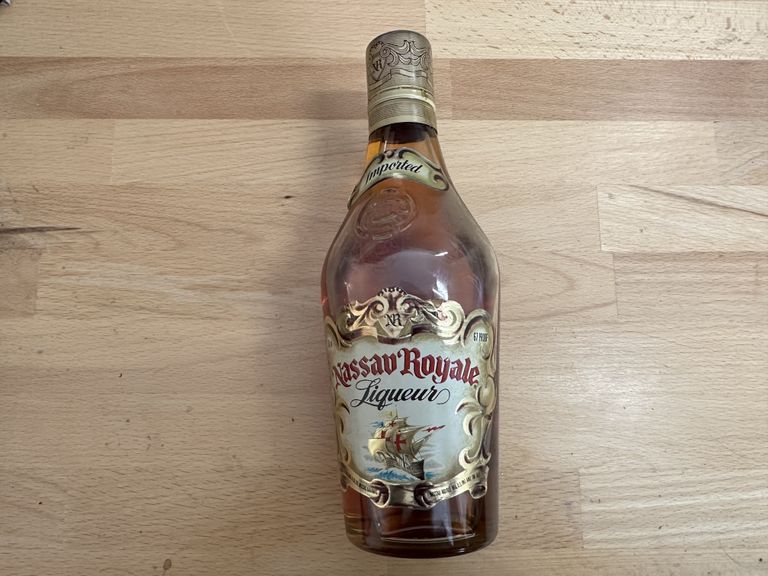 A dusty looking bottle of Nassau Royale on a wooden table.