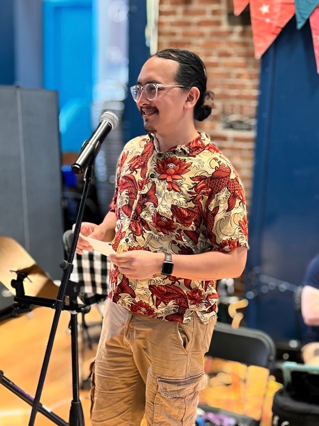 Me, wearing a red and gold patterned shirt with koi fishes on it, standing at a microphone