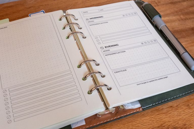 The binder open on a table: a daily page’s front on the right, and on the left the dotted “Continued” back of the previous day with its checklist
