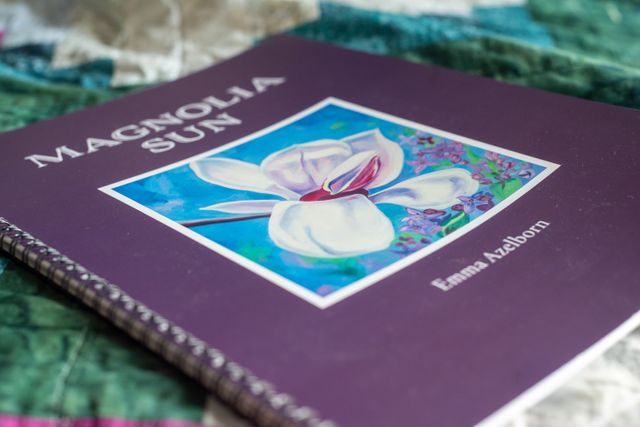 A purple songbook cover titled "Magnolia Sun" by Emma Azelborn, featuring a white magnolia flower illustration against a blue background with purple flowers.