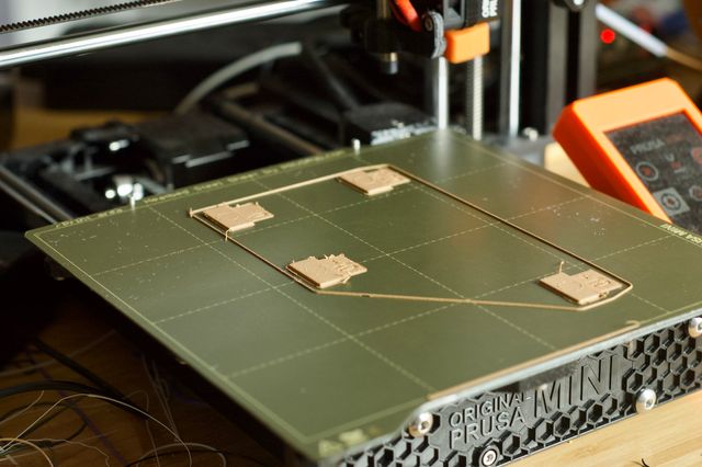 A green print bed of a Prusa MINI+ 3D printer with five small flat tan objects printed on it.