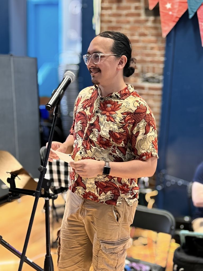 Me, wearing a red and gold patterned shirt with koi fishes on it, standing at a microphone