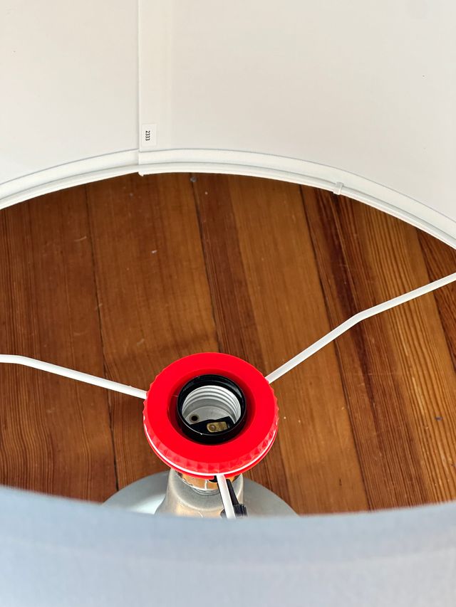 Top view of the inside of the lampshade with the red plastic bit seated around the socket of a lamp base.