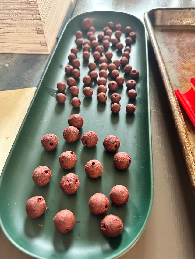 A green plastic tray full of clay beads with holes poked through.
