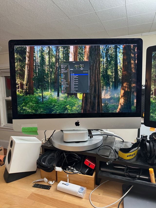 The iMac fully reassembled and showing a desktop picture of a forest with a macOS System Settings window centered on the screen.