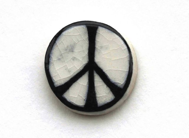 A ceramic circle with a white crackle glaze. A black peace sign is painted on it in an uneven, organic stroke. (Image from Campaign for Nuclear disarmament)