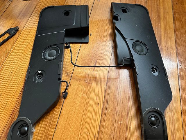 Two large, irregularly shaped, black plastic objects with two speaker drivers on each—one on the bottom and one in the middle. They appear contoured to fit in the sides of a rounded iMac chassis.