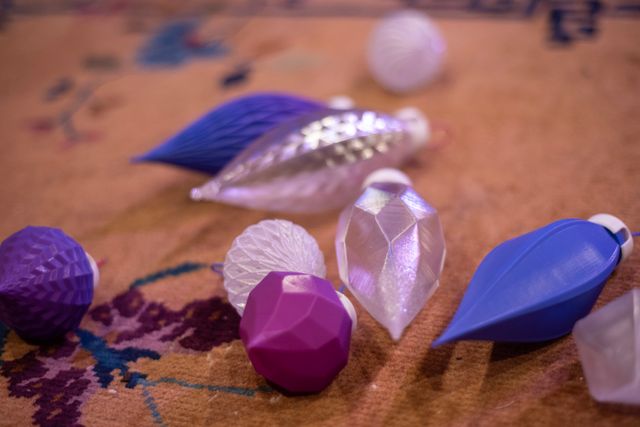 A variety of plastic Christmas ornaments strewn on a brown carpet. They are alternately clear or pink and purple. They have white caps on top.