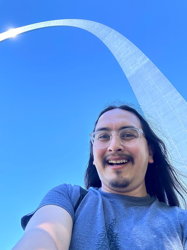 Selfie, with the St. Louis arch crossing, which gleams, crossing the image behind me, with a blue clear sky in the background.