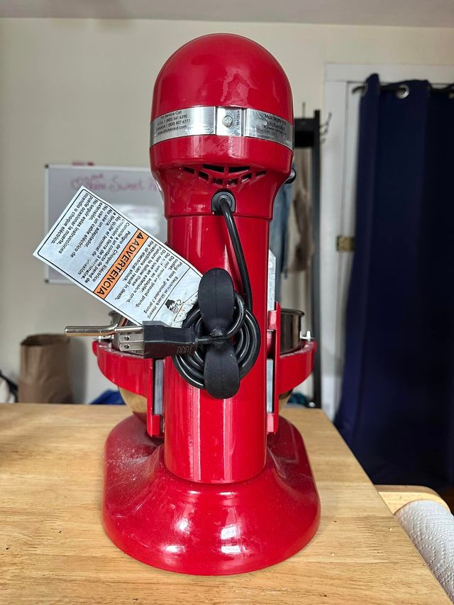 Back of a red KitchenAid stand mixer with a black silicone cable organizer adhered to the back and the power cable coiled around it.