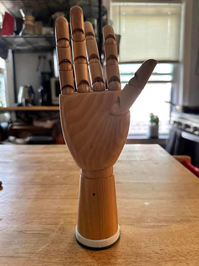 The hand and plastic piece are joined so that at the base of the articulated hand, the plastic piece is mounted flush to it. They are standing upright on the counter.