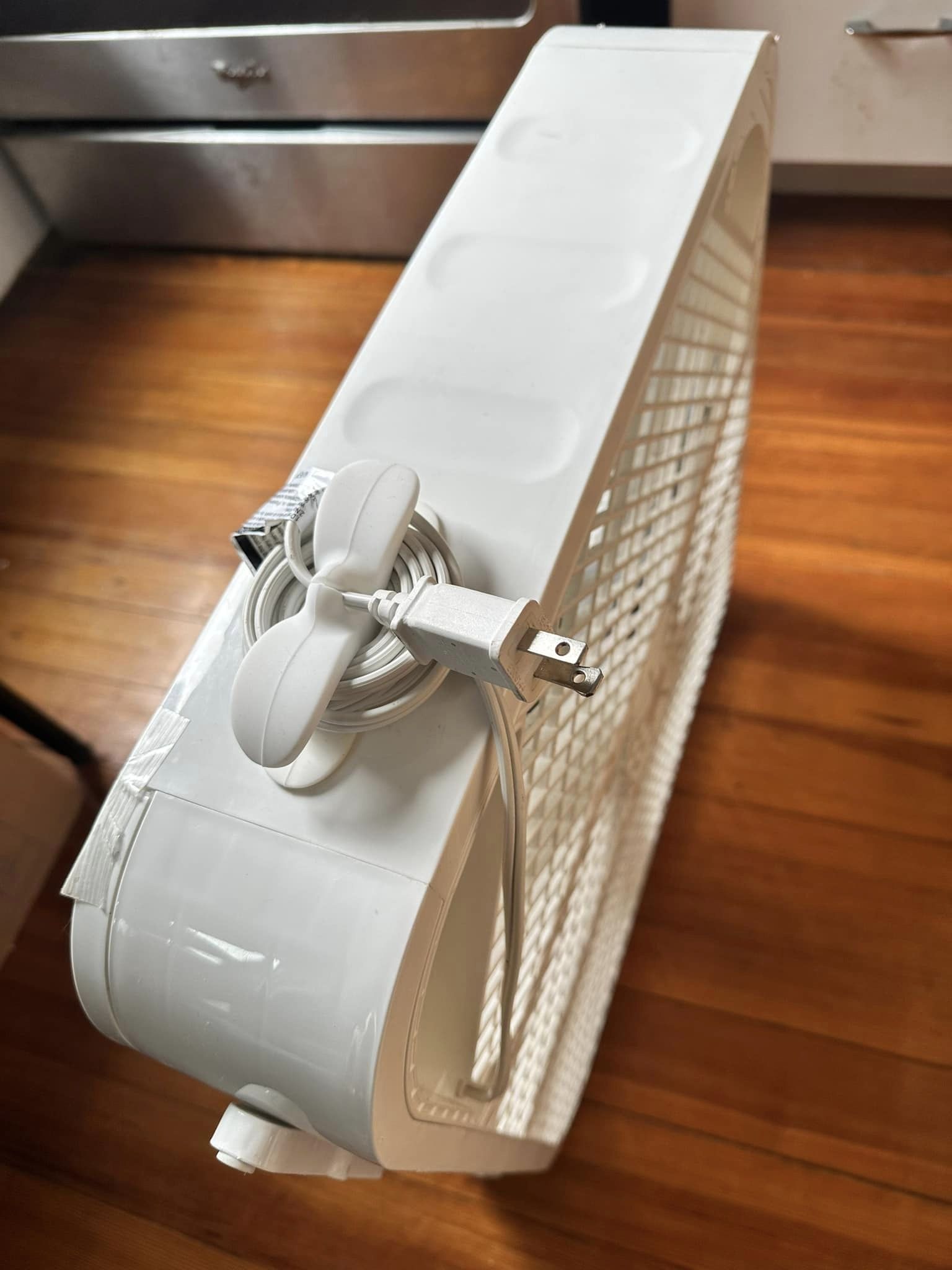 A white box fan with a white silicone cable organizer adhered to the side and the power cable coiled around it.