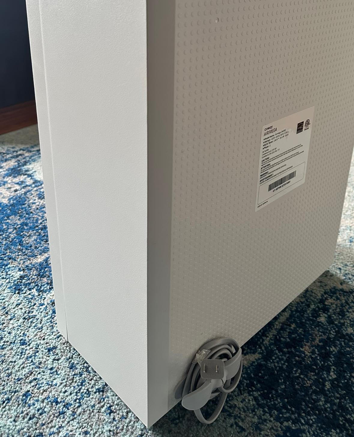 A gray boxy HEPA air purifier with a gray silicone cable organizer adhered to the back and the power cable coiled around it.